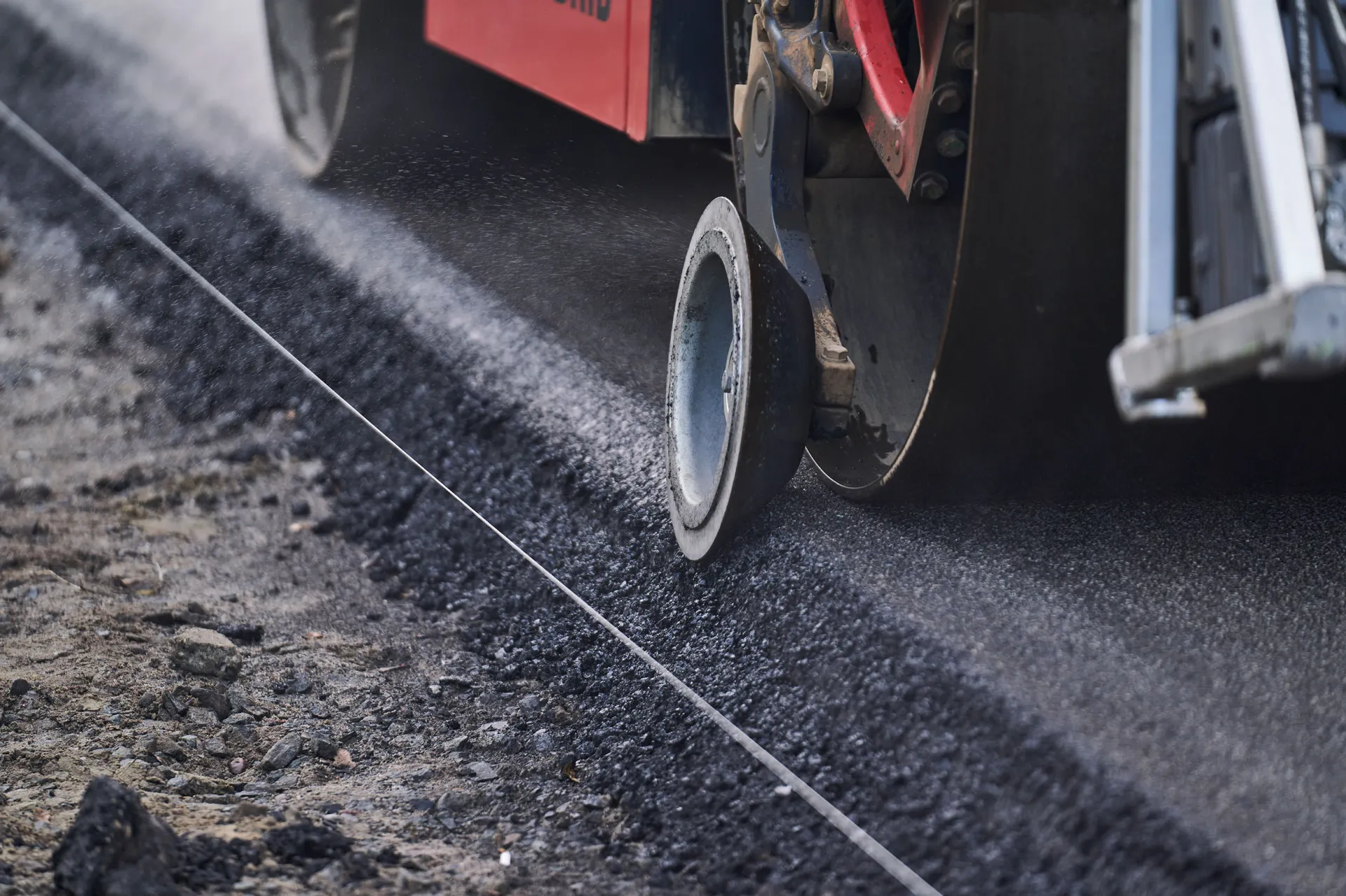 Nahaufnahme eines Straßenfertigers beim Einbau einer Asphaltkante mit gespannter Leitlinie und frischem Belag.