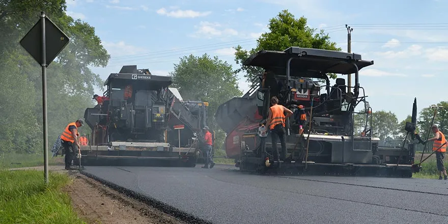 Straßenbaukolonne beim Asphaltieren einer Fahrbahn mit mehreren Maschinen und Mitarbeitenden in Warnkleidung.