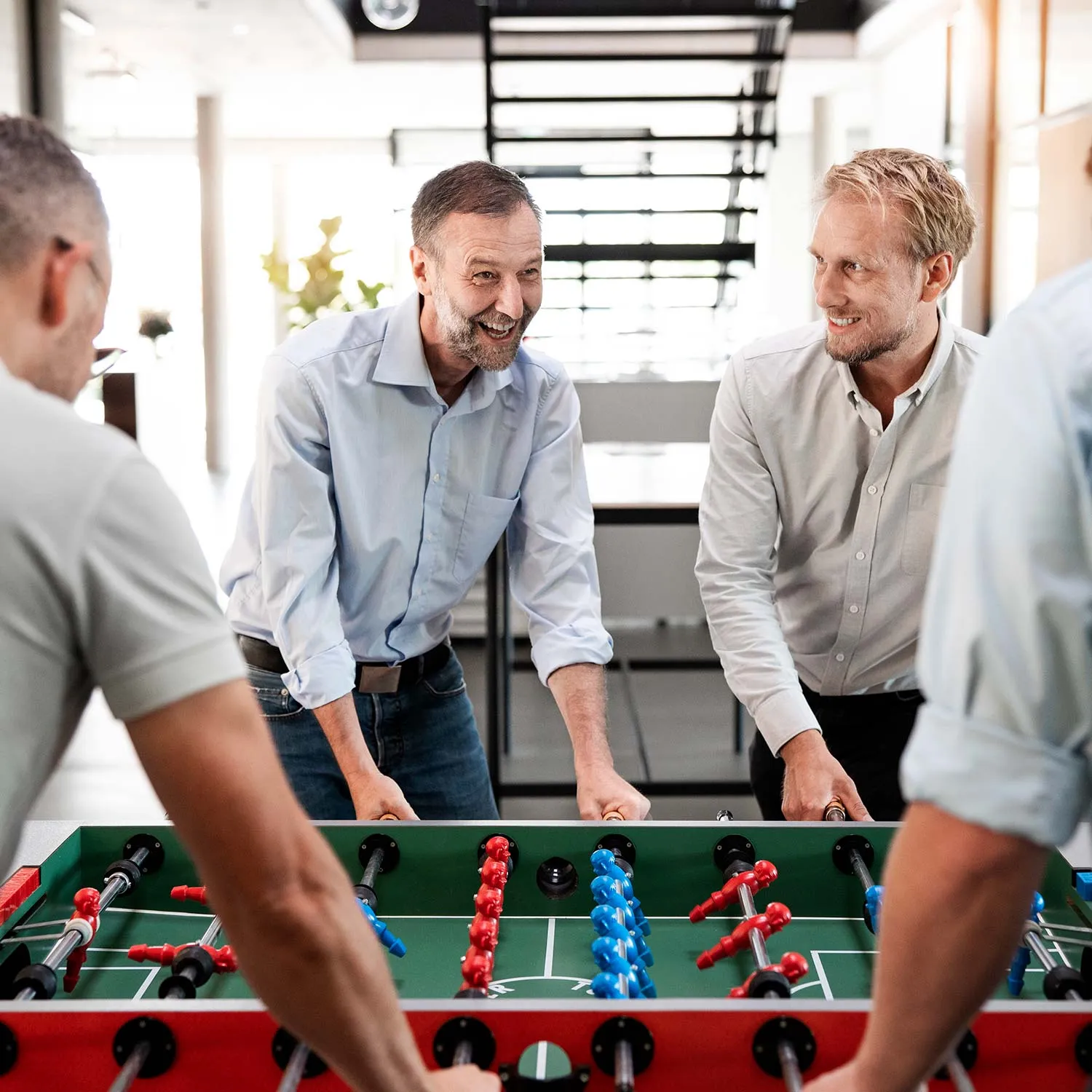 Mitarbeitende spielen gemeinsam Tischkicker im Büro