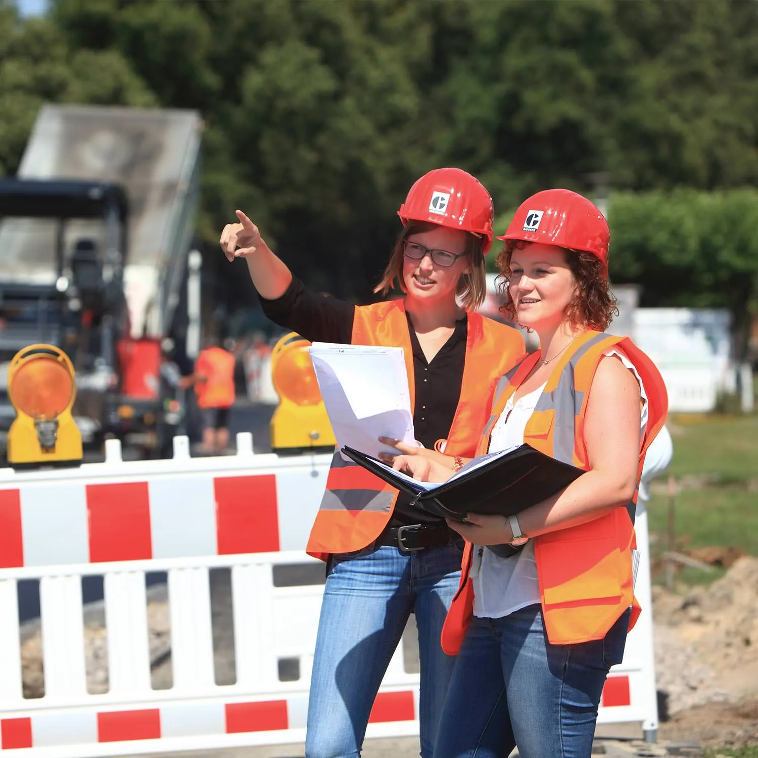 Zwei Mitarbeiterinnen mit Helm und Unterlagen auf einer Baustelle