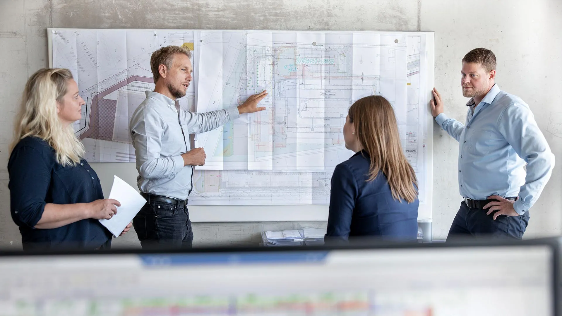 Projektbesprechung im Team vor einem großformatigen Bauplan
