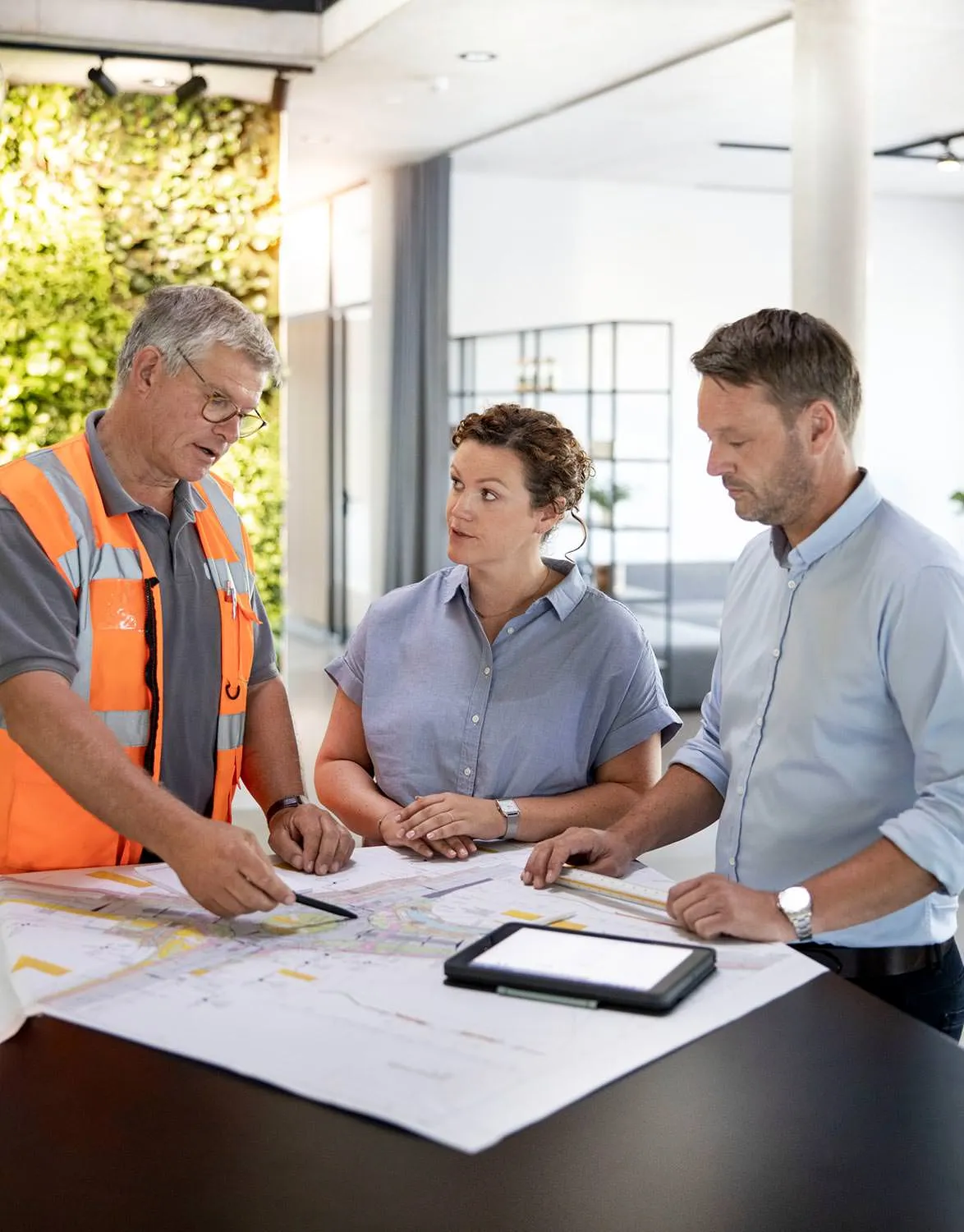 Besprechung eines Bauplans im Team mit Tablet und Unterlagen