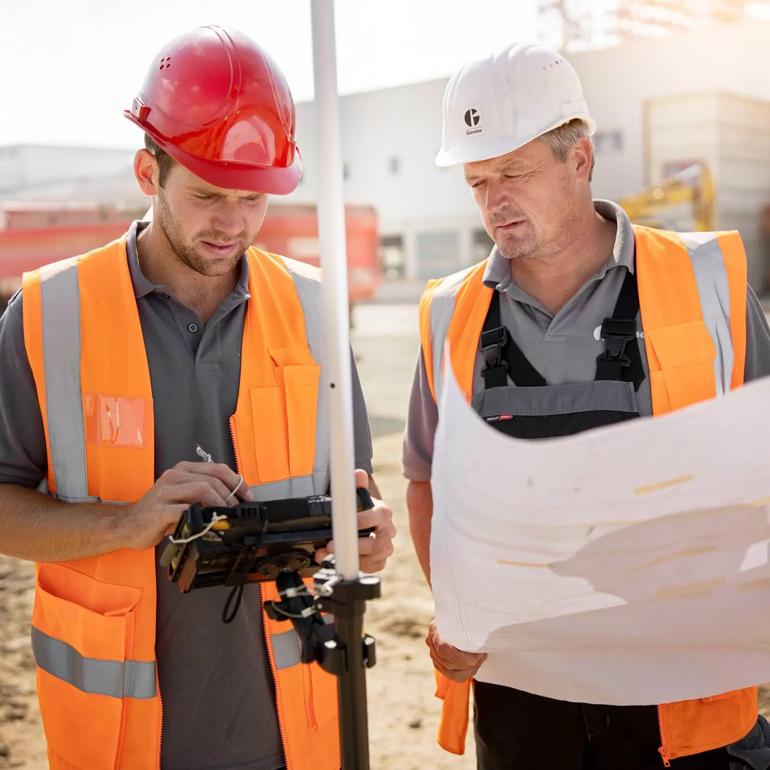 Zwei Mitarbeiter mit Vermessungstechnik und Bauplan auf der Baustelle