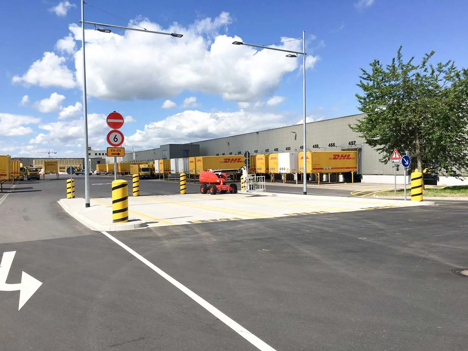 Verkehrsfläche an einer DHL-Verladehalle mit Fahrbahnmarkierungen, Pollern und abgestellten Wechselbrücken.