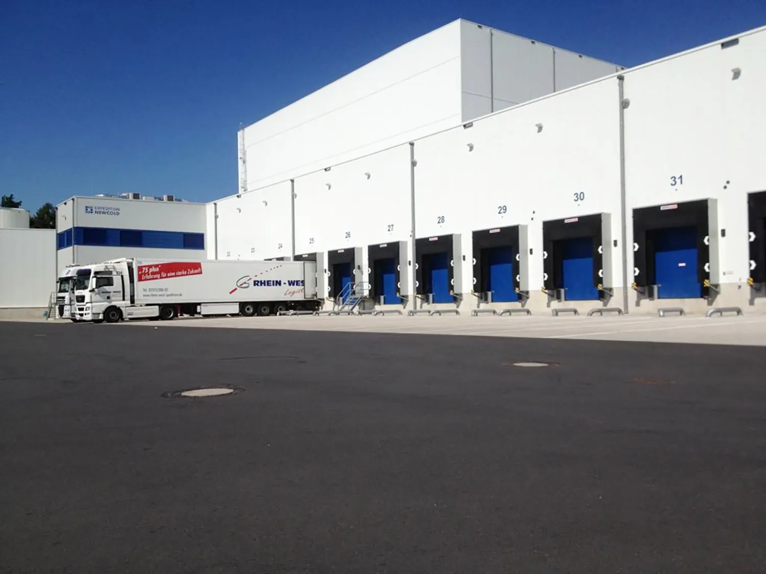 Logistikhalle mit mehreren Verladetoren und angedocktem Sattelzug auf großer Rangierfläche.