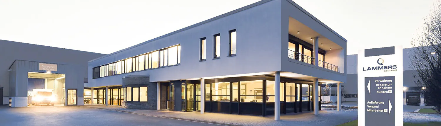 Modernes Verwaltungsgebäude mit beleuchteter Glasfassade und überdachtem Eingangsbereich.