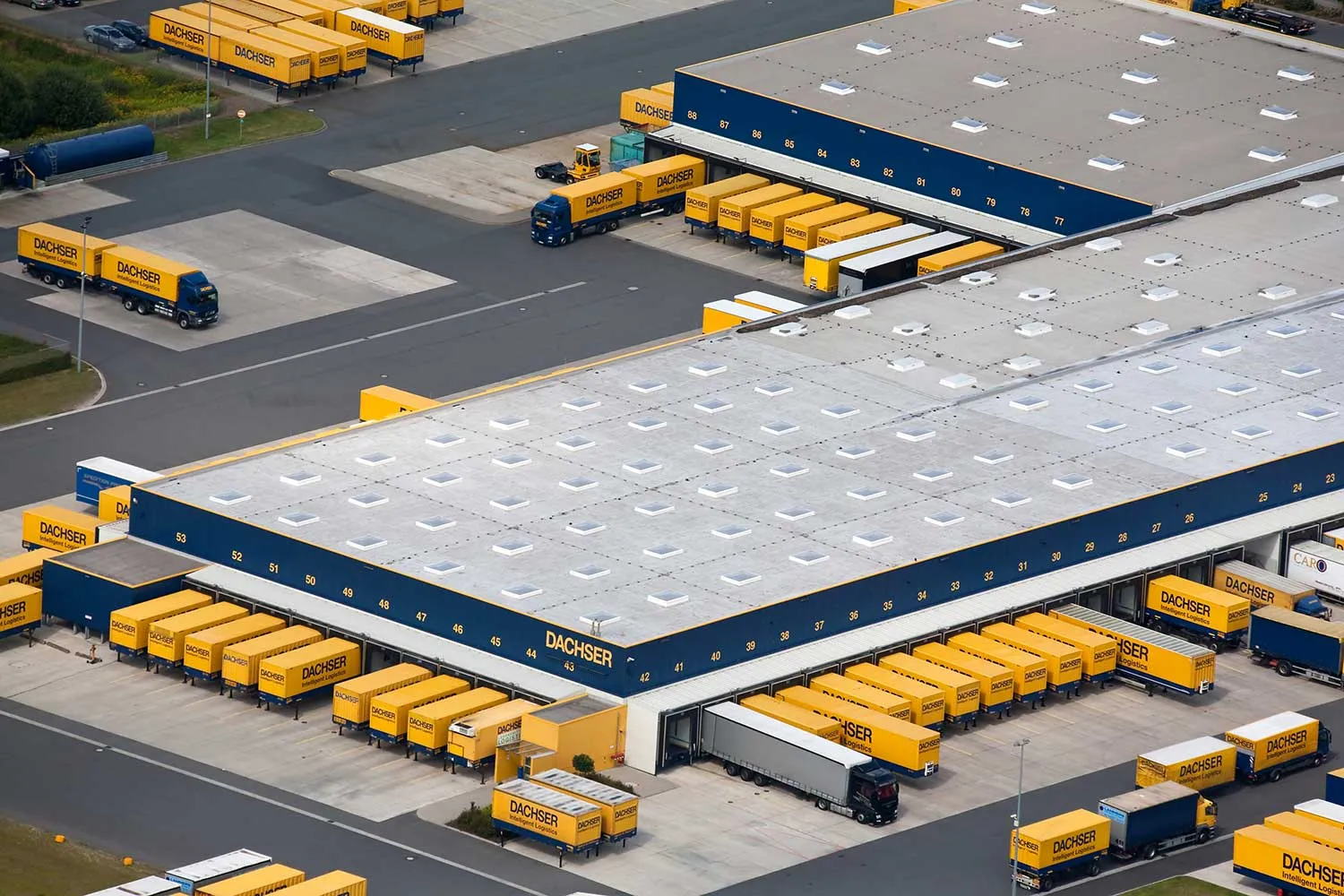 Luftaufnahme eines Dachser-Logistikzentrums mit Verladezonen, Hallendach und gelben Wechselbrücken.
