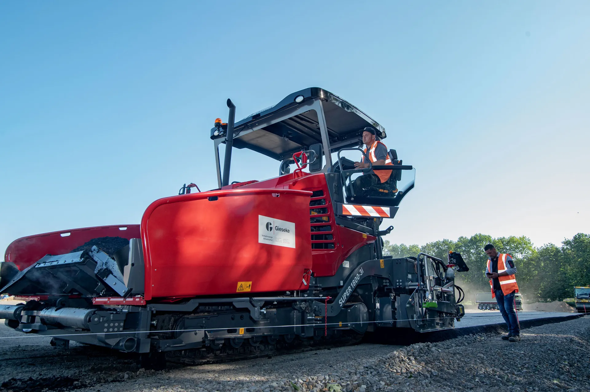 Asphaltfertiger mit Mitarbeitenden im Einsatz auf einer Straßenbaustelle