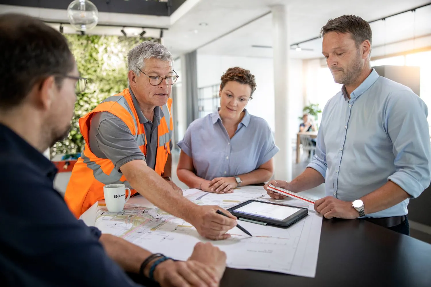 Besprechung eines Bauplans im Team mit Tablet und Unterlagen