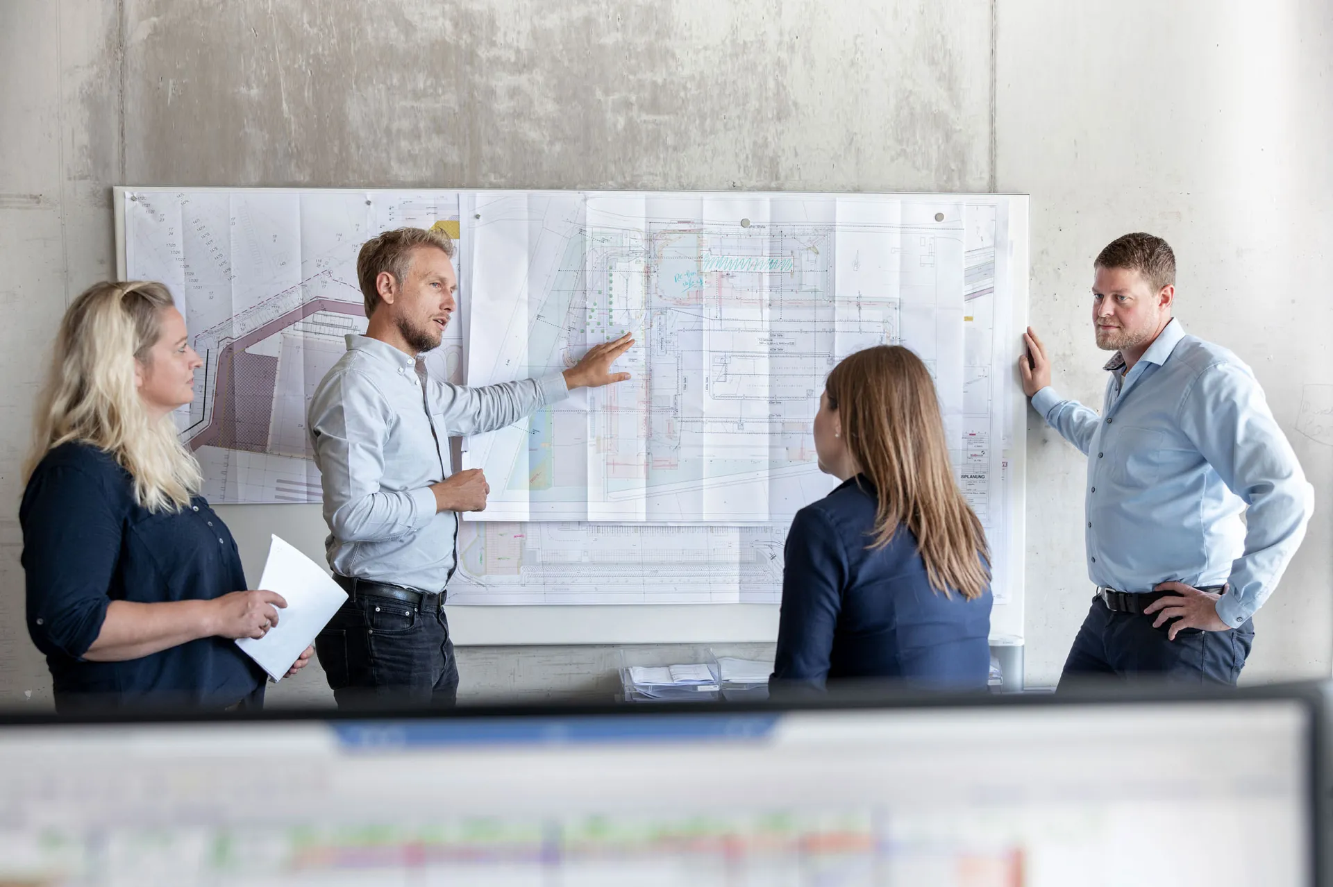 Projektbesprechung im Team vor einem großformatigen Bauplan