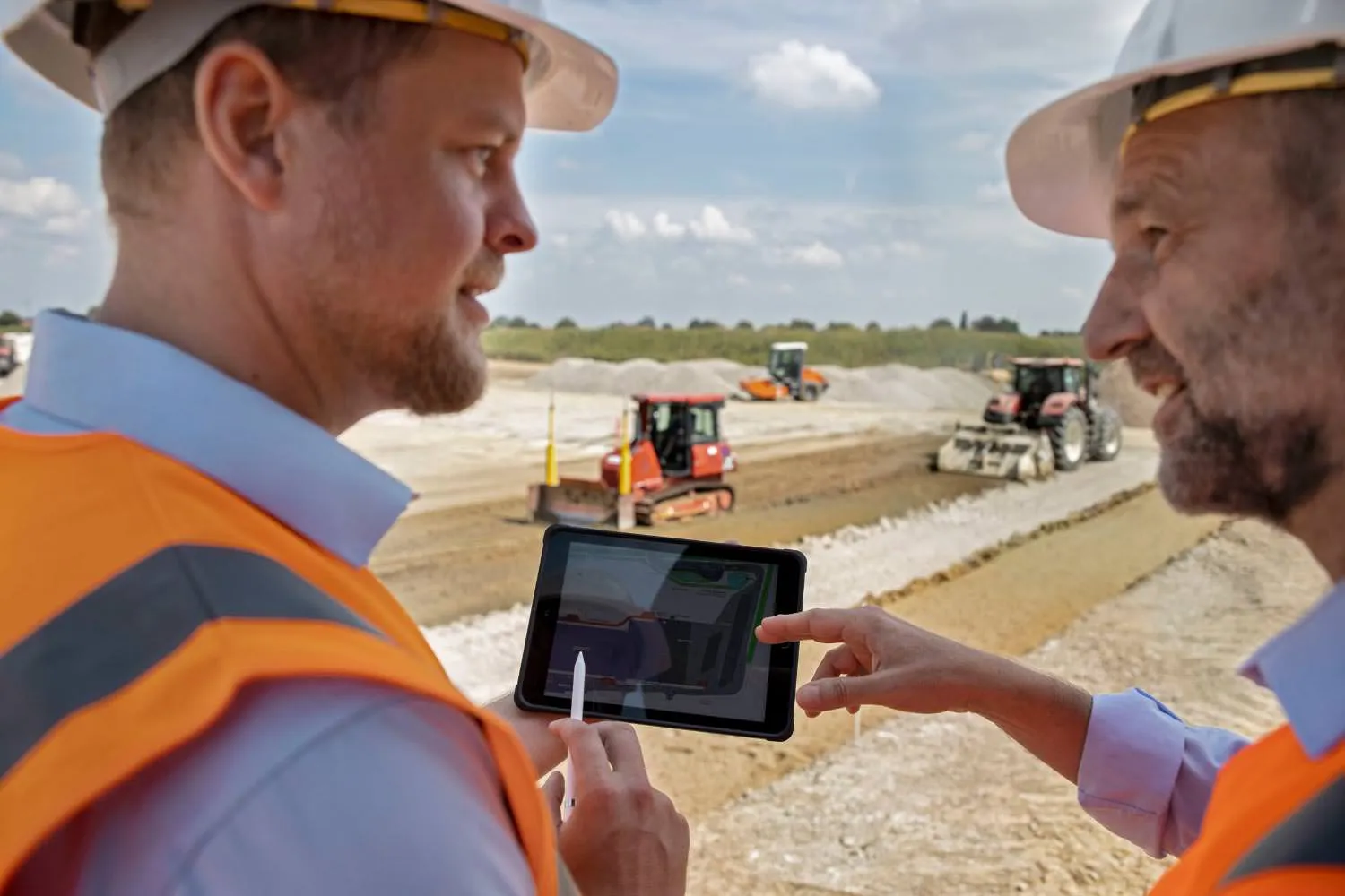 Zwei Menschen auf einer Baustelle mit Tablet vor Baumaschinen