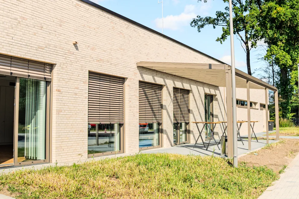 Modernes eingeschossiges Gebäude mit heller Klinkerfassade, Fenstern und überdachtem Eingangsbereich an einem sonnigen Tag
