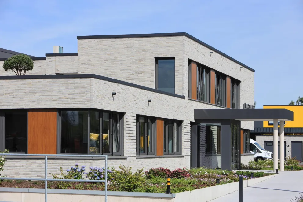 Modernes zweigeschossiges Gebäude mit heller Klinkerfassade, großen Fenstern und gepflegter Grünanlage.