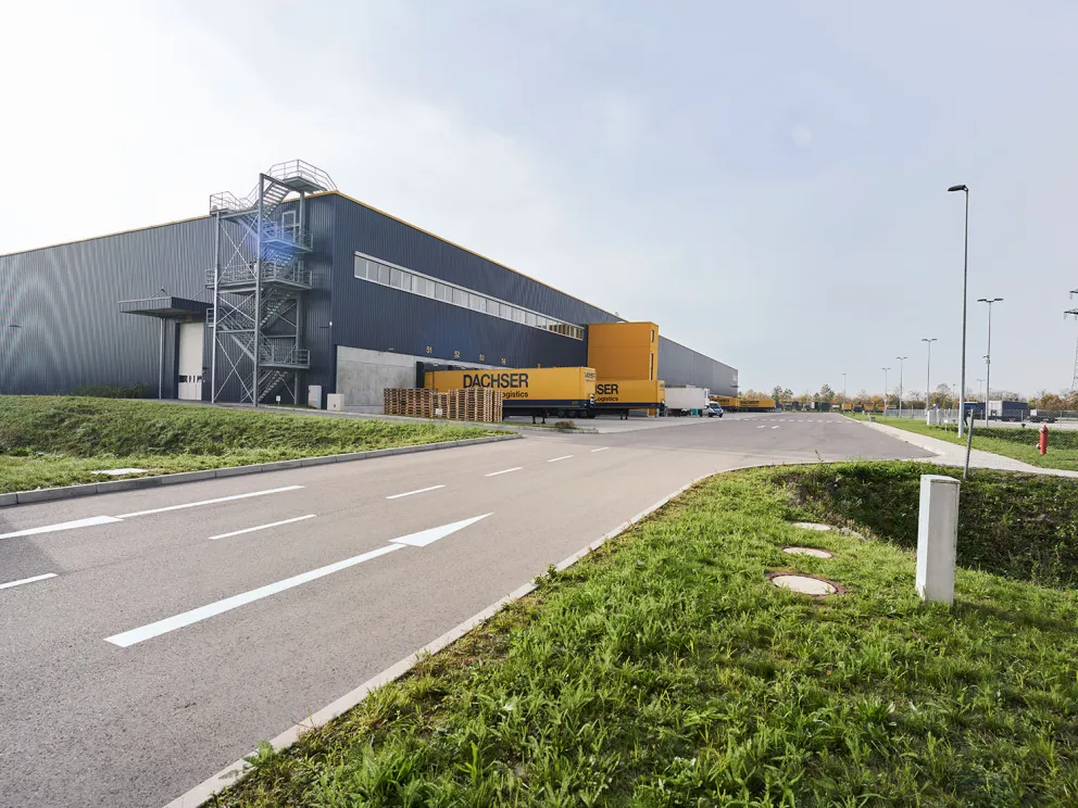 Straßenansicht eines Dachser-Logistikzentrums mit Hallengebäude und Erschließungsstraße.